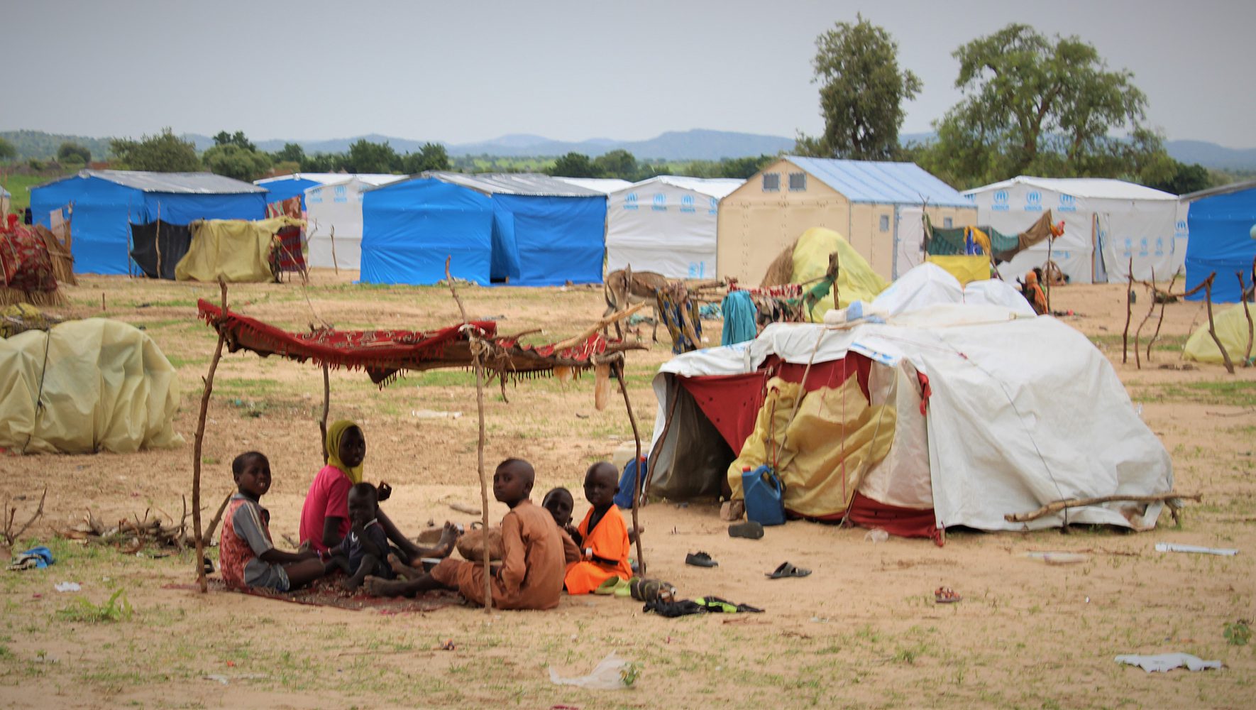 Sudanese refugee families with children in a displacement camp with UNHCR tents